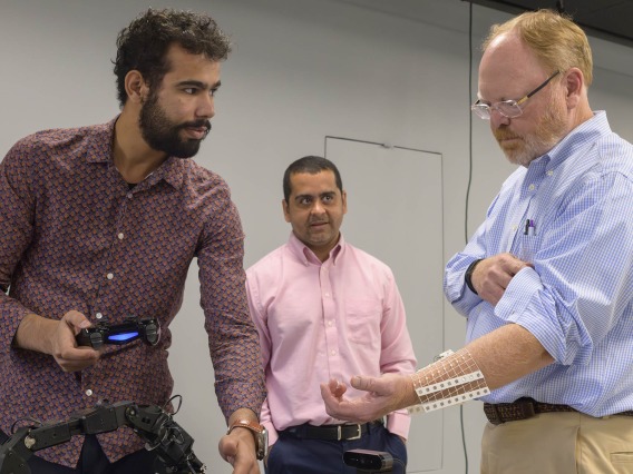 (From left) Qusai Almustafa, a SensorLab intern, and Gustavo Almeida, PhD, SensorLab manager and former UArizona Health Sciences Data Science Fellow, demonstrate how wearable sensors enable Wes Gullett, director of operations for the WearTech Center in Phoenix, operate a robotic arm in the UArizona Health Sciences SensorLab during a tour sponsored by the Greater Phoenix Economic Council.  