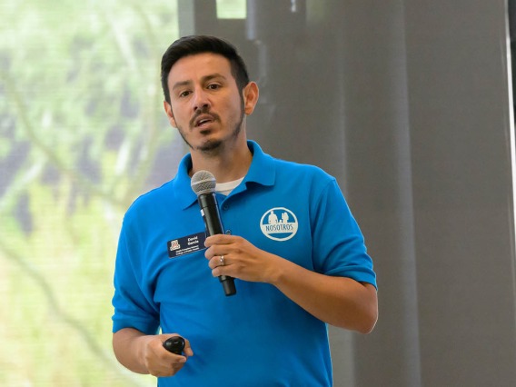 David O. Garcia, a Hispanic man with dark hair and a blue polo shirt, holding a microphone talking. 