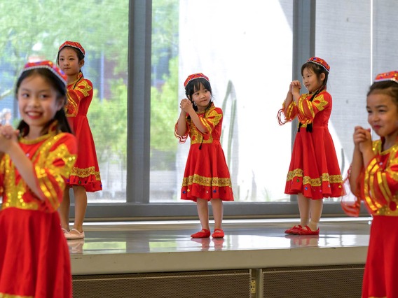 Several young girls from the Tucson Chinese Dance group wear colorful red and gold dresses while performing a dance.