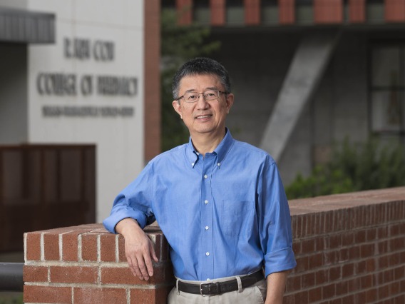 Portrait of Dr. Xinxin Ding standing outside leaning on a red brick wall. 