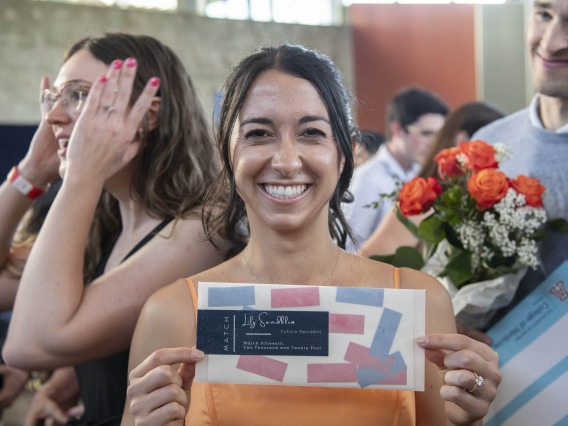 A female, fourth-year medical student from the University of Arizona College of Medicine – Phoenix smiles as she holds up an envelope containing information about where she matched for her residency. 