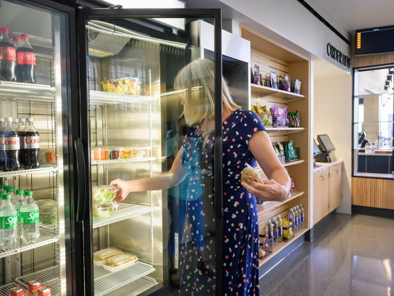 A woman reaches into a refrigerated case to grab a salad in the cafe. 