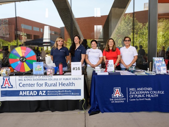 Five women stand behind information tables with banners for the UArizona Center for Rural Health. 