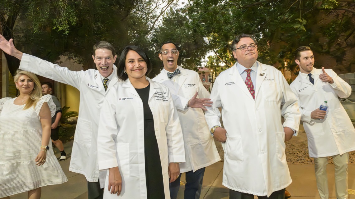 Six college of medicine faculty members wearing white coats and acting silly walk outside on their way to the white coat ceremony. 