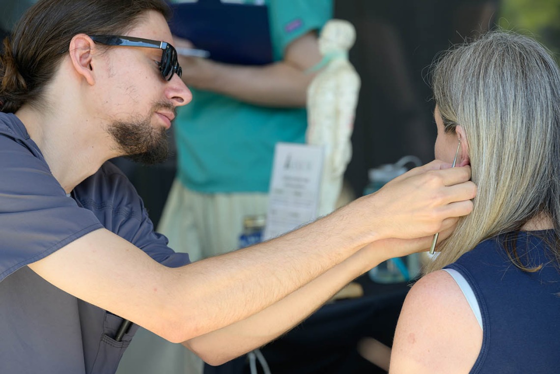 A man attaches a small taped bead to the ear of a woman with long gray hair. 