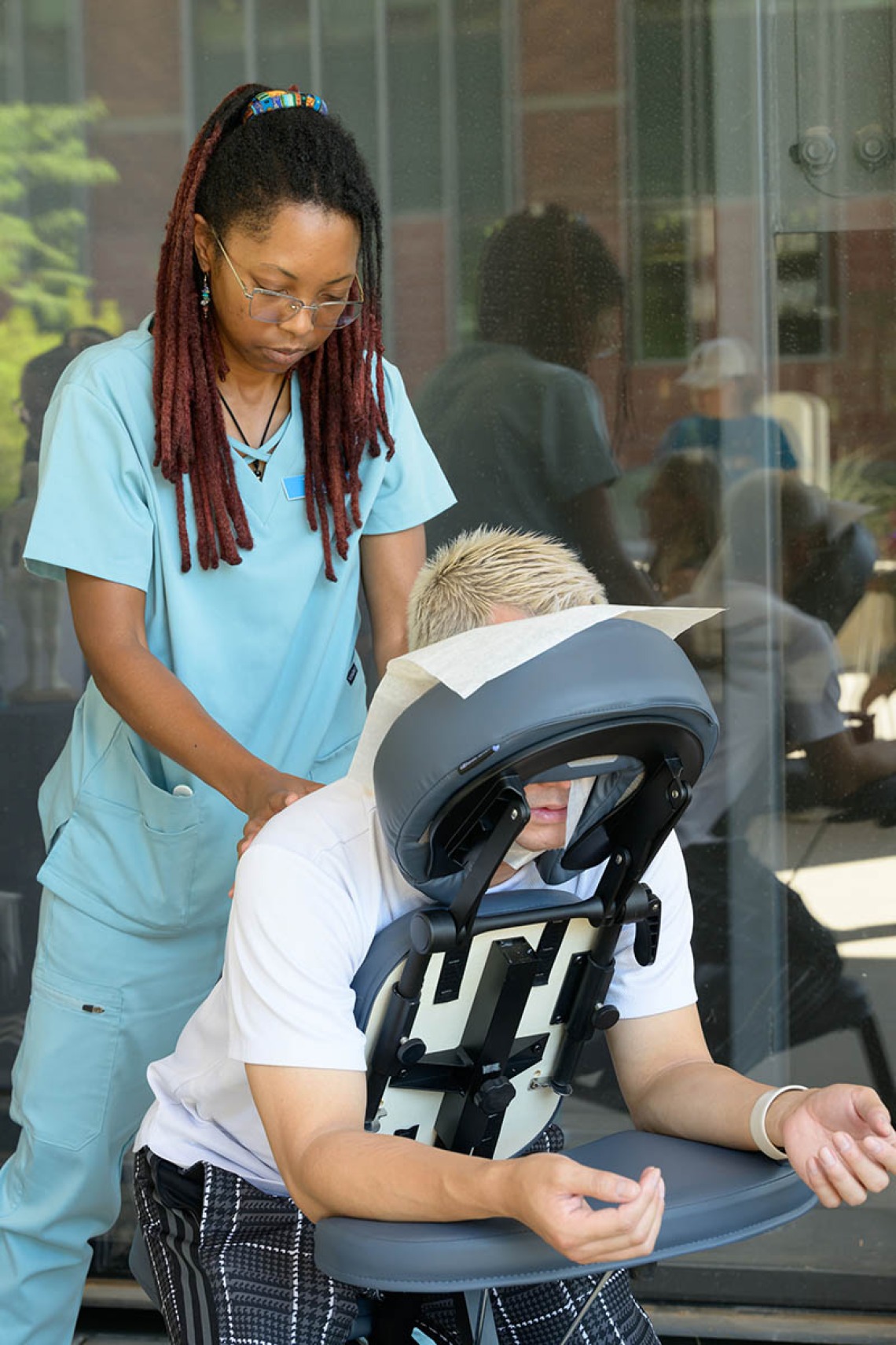 A woman dressed in scrubs gives a chair massage to a person with gray hair. 