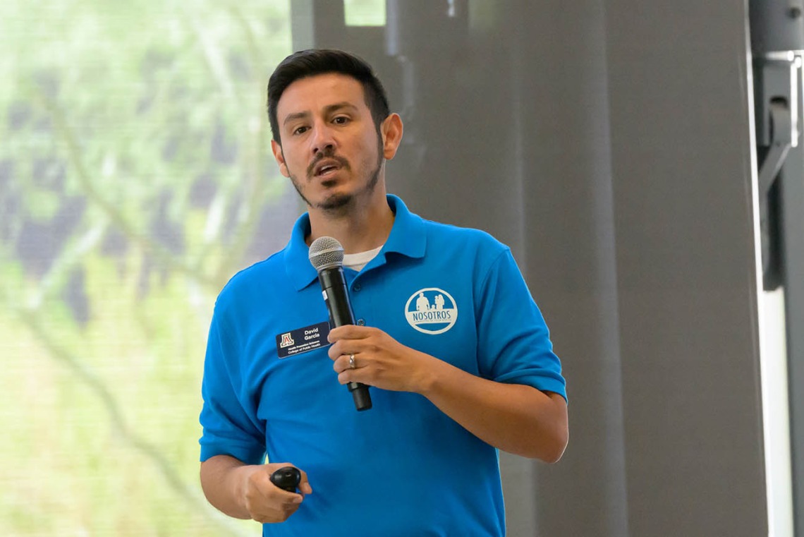 David O. Garcia, a Hispanic man with dark hair and a blue polo shirt, holding a microphone talking. 