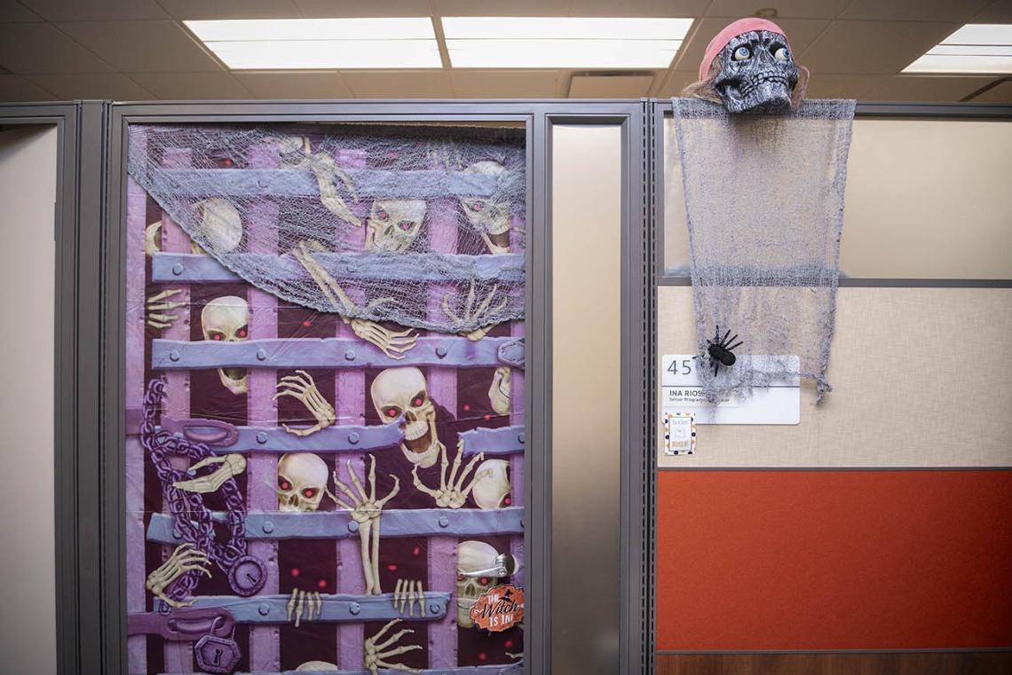 A cubicle wall with an image of an iron gate with skeletons trying to get through it. 