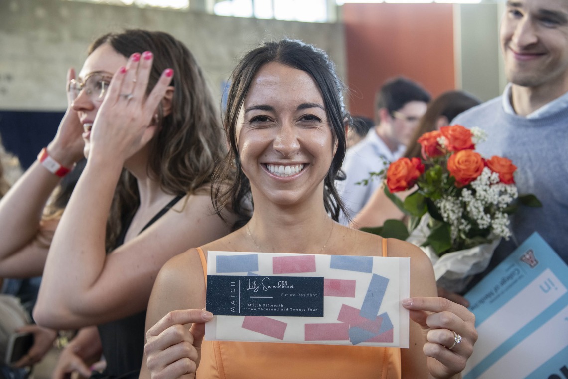 A female, fourth-year medical student from the University of Arizona College of Medicine – Phoenix smiles as she holds up an envelope containing information about where she matched for her residency. 