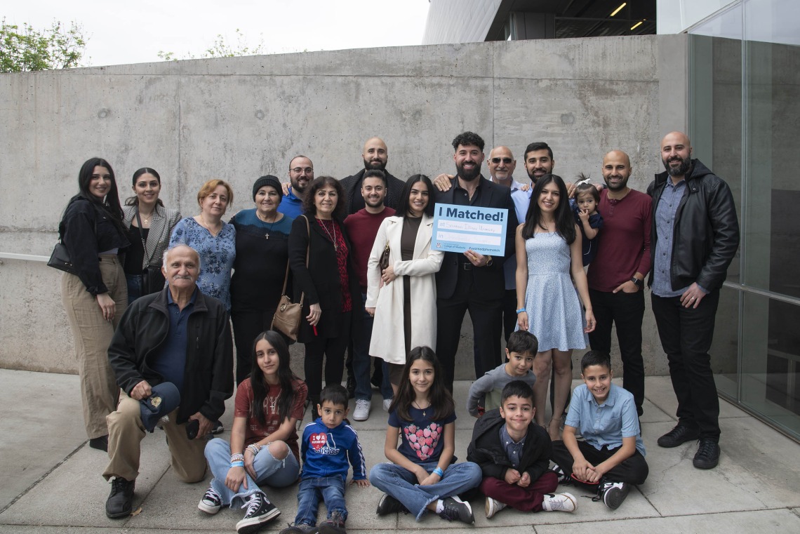 A group of more than 20 family members stand with a University of Arizona College of Medicine – Phoenix medical student who holds an “I Matched” sign. 