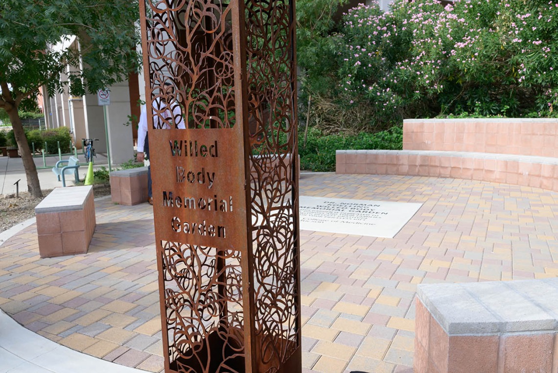 A decorative metal sign post in a garden says, "Willed body memorial garden". 