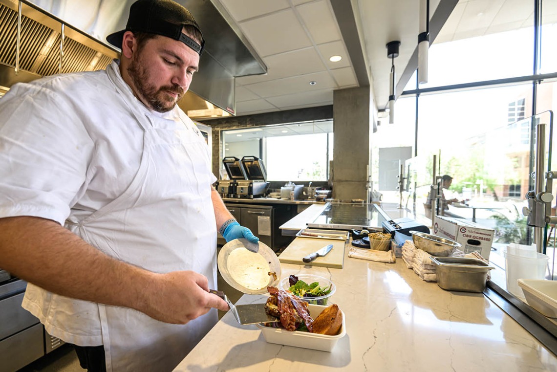 A male chef with a white coat puts food onto a tray on a counter.