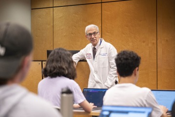 Older man with glasses and white hair speaks to a class in a lecture hall.