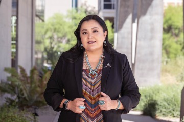 Native American woman wearing a traditional tribal blouse and turquoise necklace and a black blazer on top.