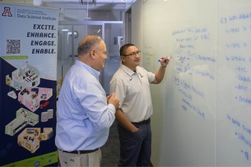 two men stand at white board
