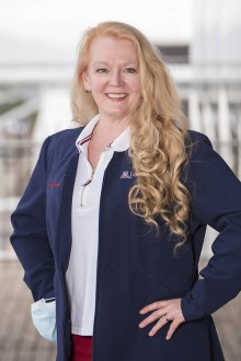 Woman with long blonde hair with hands on hips wearing a blue blazer. She is smiling. 